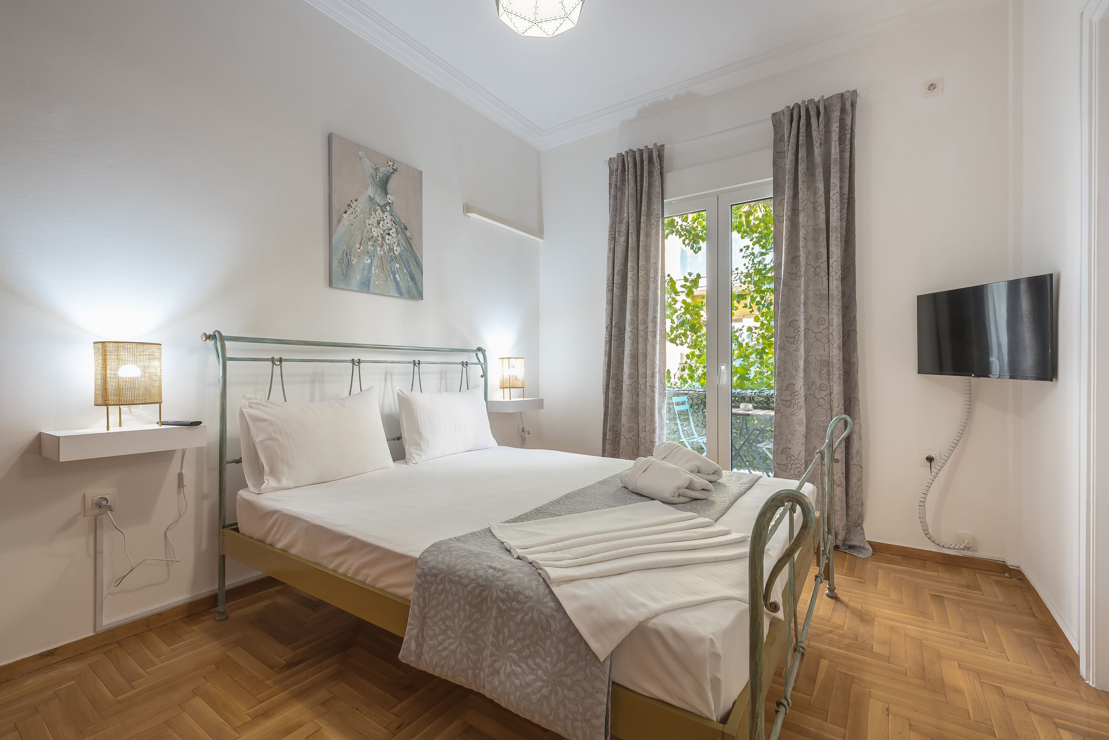 A bedroom with a bed, bedside lamps, a TV, and a window with curtains.