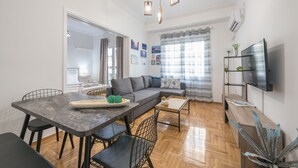 A modern living room with a dining area, a sofa, a TV, and a wooden floor. - Athens Bright Suite by Cloudkeys (Athens)