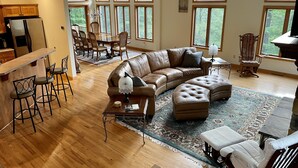 A spacious living room with a large sectional sofa, a dining area with wooden chairs, and a kitchen with a refrigerator.