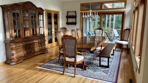 A dining room with a large wooden table, matching chairs, a bench, a chandelier, and a large wooden cabinet with glass doors.