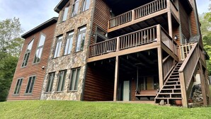 A multi-story log cabin with a stone facade, a balcony, and a staircase leading to an upper level.