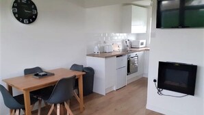 A compact living space with a dining area, kitchenette, and a TV mounted on the wall.