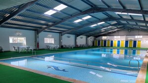 An indoor swimming pool with a diving board, surrounded by green artificial turf and a row of colorful doors.