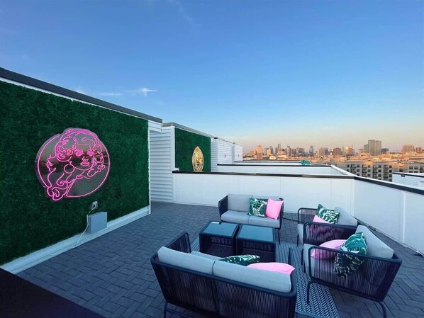 A rooftop terrace with outdoor seating and a neon sign on the wall.