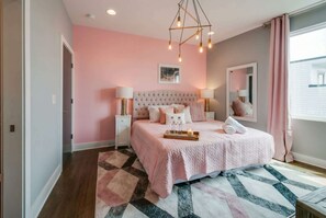 A bedroom with a tufted headboard, a pink bedspread, bedside lamps, and a geometric-patterned rug.