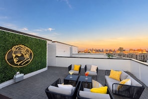 A rooftop terrace with outdoor seating, a neon portrait, and a city skyline view. - Fall Nashville getaway: 2 rooftop homes, karaoke rooms, sleeps 24 (Nashville)