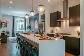 A modern kitchen with a central island, bar stools, pendant lighting, and a large mural.