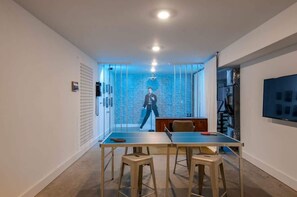 A modern room with a ping pong table, a TV, and a brick wall with a person in the background.