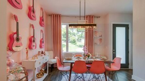 Ein Essbereich mit einem Tisch für vier Personen, rosa Stühlen, einem weißen Schrank und Gitarren an der Wand.