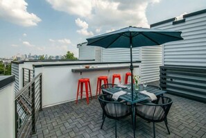 Terraço no topo com mesa, cadeiras, um guarda-sol verde e banquetas vermelhas.
