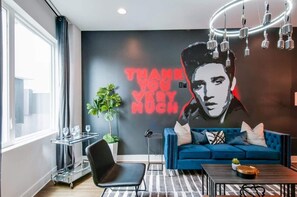 A modern living room with a blue sofa, a glass coffee table, and a neon sign on the wall.