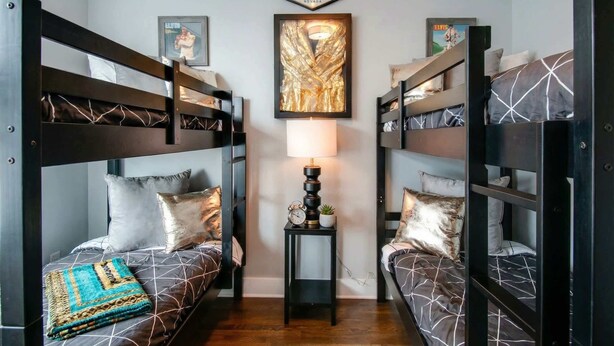 Ein Zimmer mit Etagenbetten, einem Willkommensschild, einem gerahmten Kunstwerk und einem kleinen Tisch mit einer Lampe.