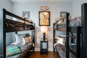 A room with bunk beds, a welcome sign, a framed artwork, and a small table with a lamp.