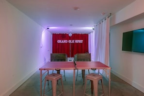 A room with a red curtain, a table with four stools, and a flat-screen TV mounted on the wall.