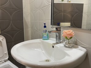 Ett badrum med ett vitt handfat, en spegel och en flaska lotion.