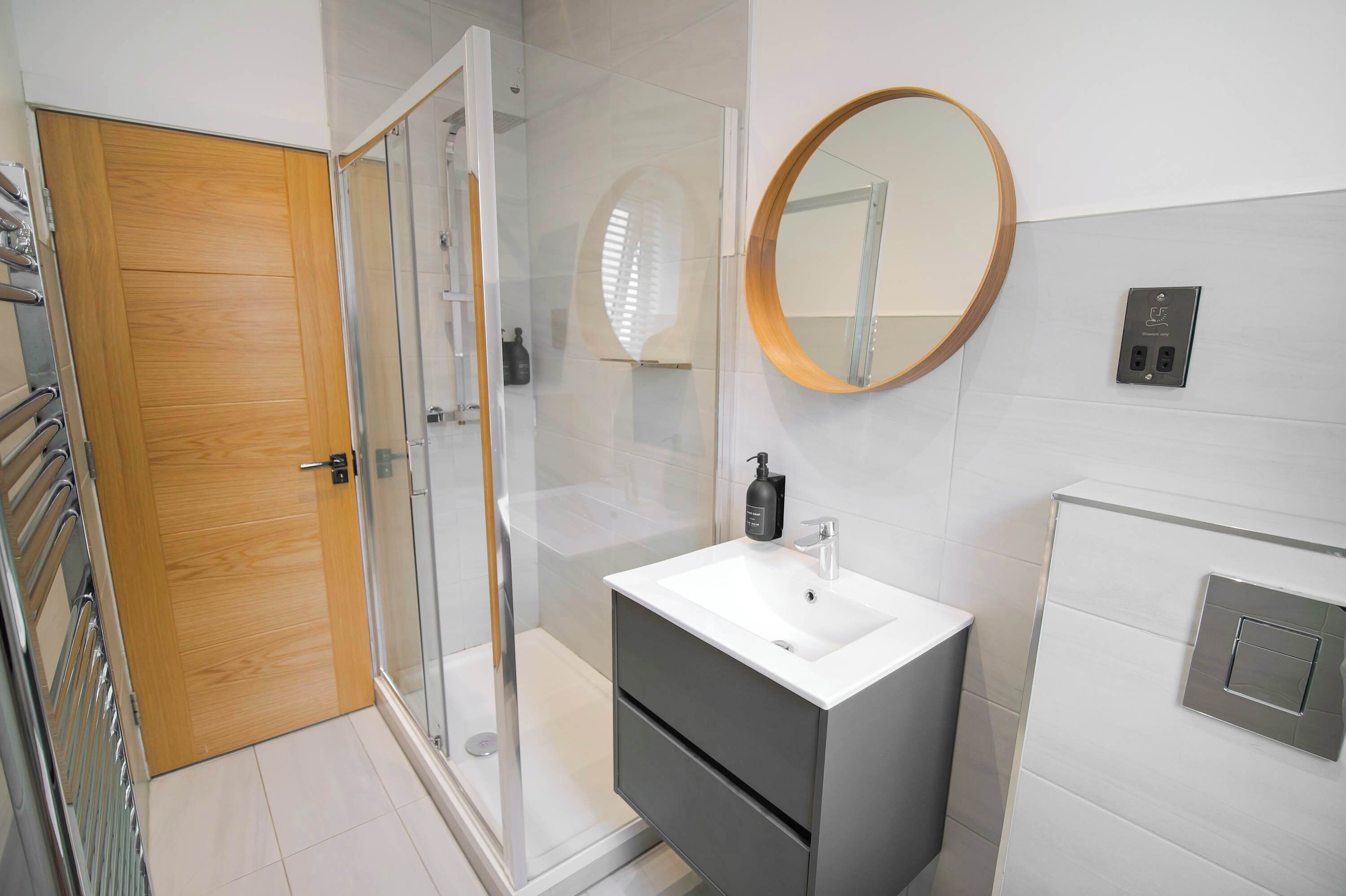 A modern bathroom with a glass shower enclosure, a white sink, and a wooden door.