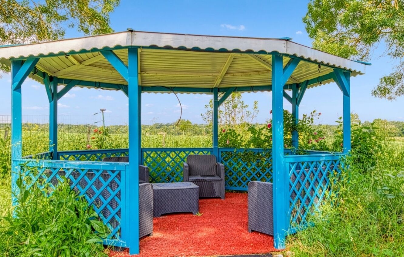 Gazebo con ringhiere a reticolo blu e tappeto rosso, circondato da vegetazione.
