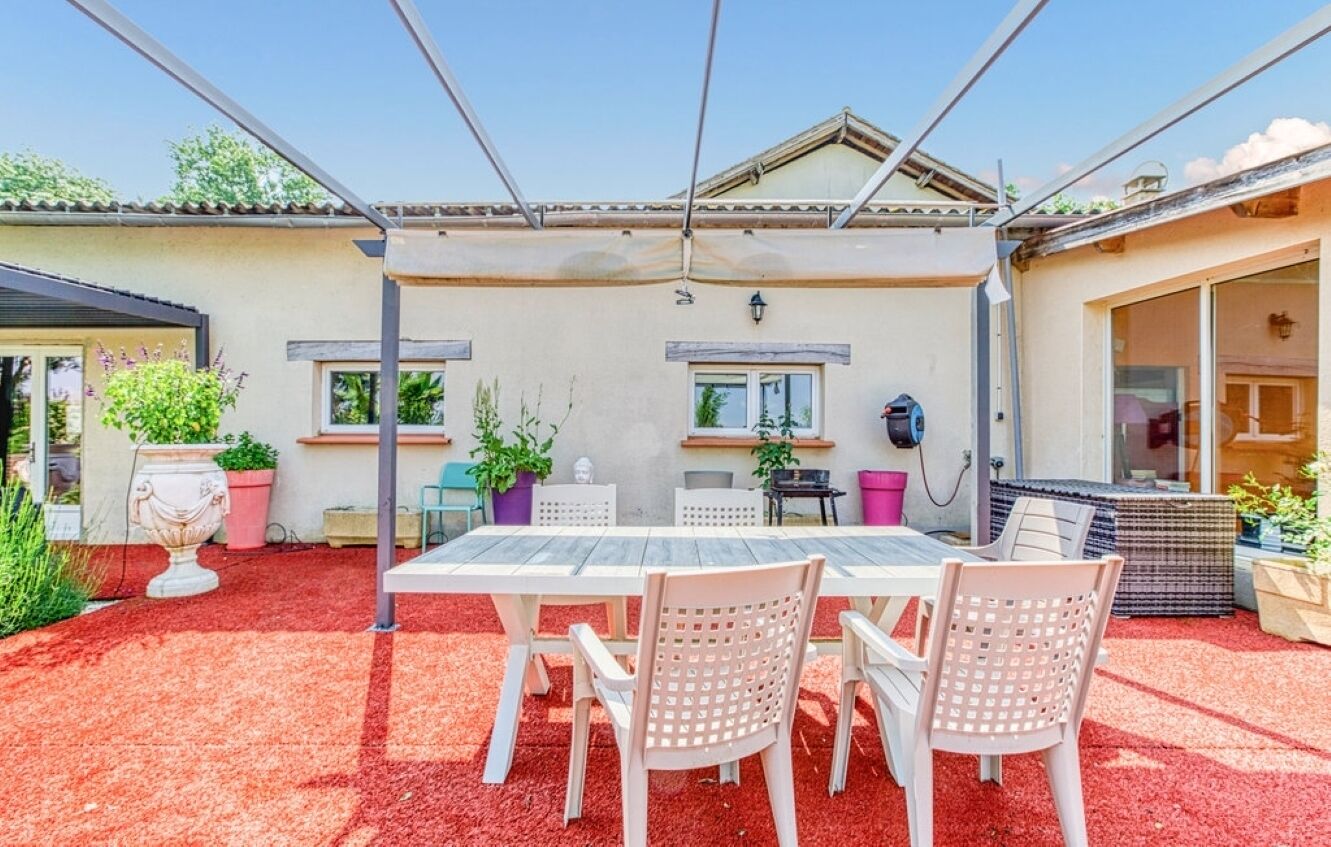 A covered patio with a table and chairs, potted plants, and a pergola structure.