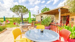 A patio with a round glass table and chairs, surrounded by potted plants and a stone building. - Pleasant studio of the Daudou with shared swimming pool and jacuzzi. (Septfonds)