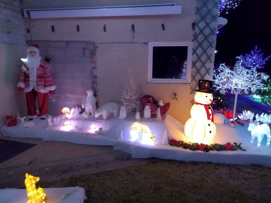 Uma casa decorada com luzes de Natal, incluindo um boneco de neve, renas e o Papai Noel.