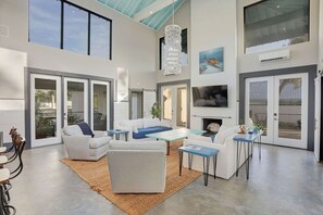 Amplia sala de estar con techos altos, ventanas grandes, chimenea y televisor de pantalla plana.