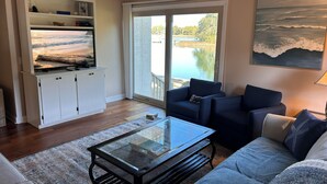 A living room with a glass coffee table, a sofa, a chair, a white cabinet, and a large window with a view of a body of water. - South Beach Dog-friendly Waterfront Villa (Hilton Head Island)
