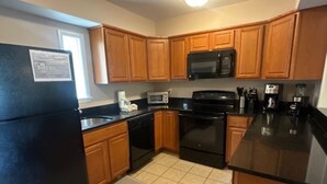 A compact kitchen with wooden cabinets, a black refrigerator, a microwave, a stove, and a coffee maker. - South Beach Dog-friendly Waterfront Villa (Hilton Head Island)