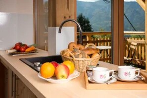 A kitchen with a sink, a fruit bowl with apples and oranges, a basket of bread, and a tray with cups and saucers. - Lärche Vacation Home (Bad Goisern am Hallstättersee)
