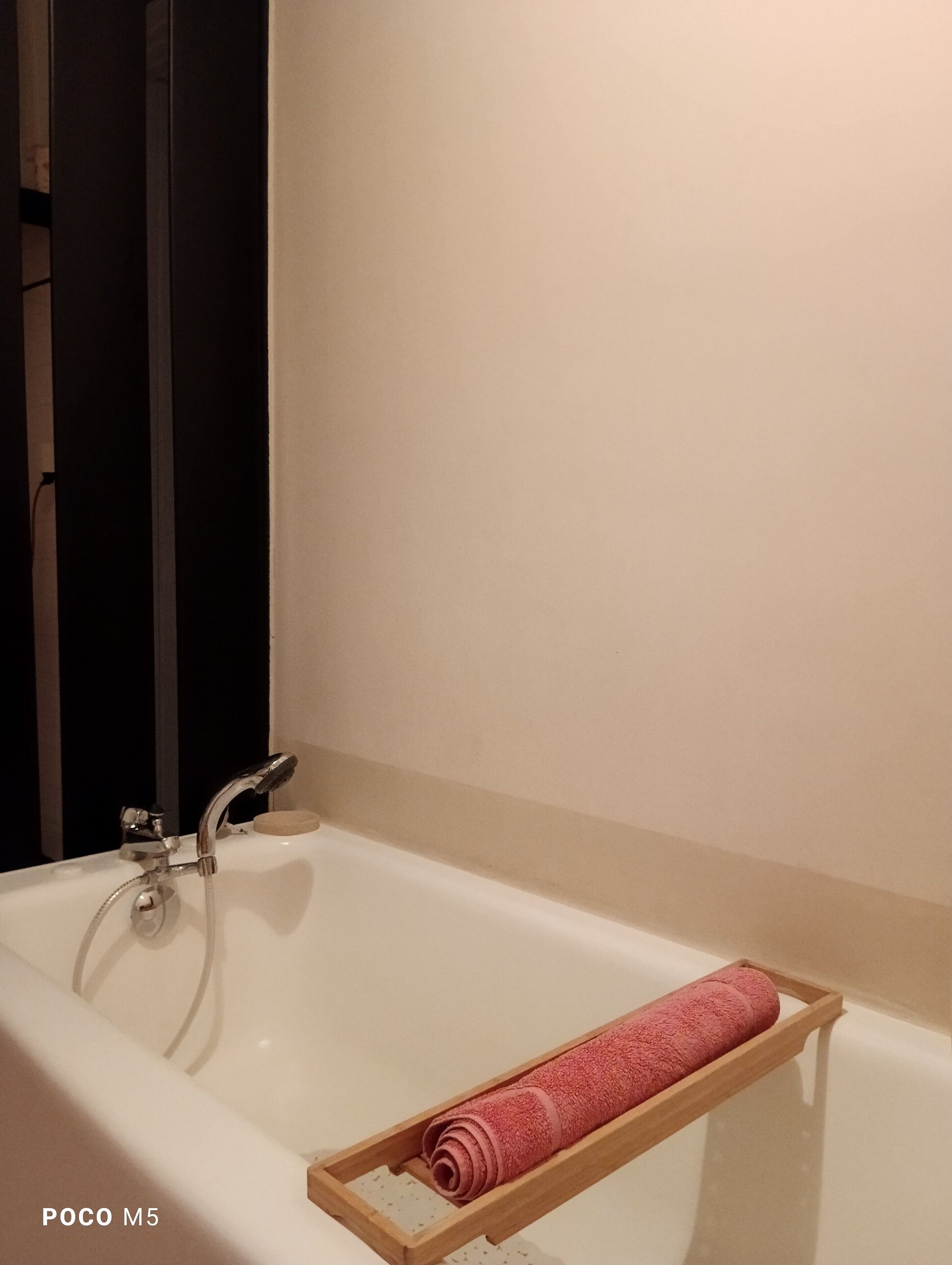 Un baño con una bañera blanca, un perchero de madera y una pared color crema.
