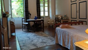 A room with a bed, a desk, a chair, and a window with curtains. - Large bedroom (3 + 1 baby ) & Dining area in a country village -  (Lézat-sur-Lèze)
