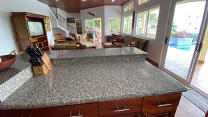 A kitchen with granite countertops, wooden cabinets, and a dining area with a sofa and chairs. - Perfect viewing of migrating Pacific whales, from the hills above Ojochal (Ojochal)