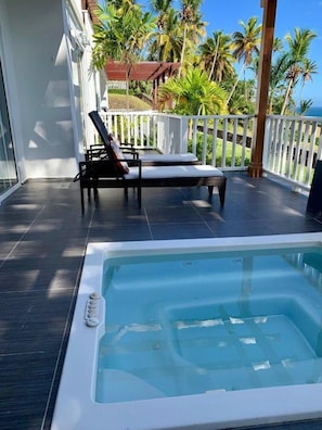 A pool area with a hot tub, lounge chairs, and a view of palm trees and a building in the background.