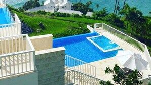 A resort with a pool, a view of the ocean, and palm trees.