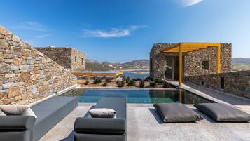 A rooftop pool area with stone walls, lounge chairs, and a view of the sea and mountains.