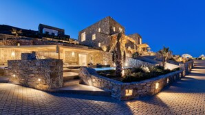 A stone building with a pool, stone walls, and a paved area. - Panormos Bay Suites (Mykonos)