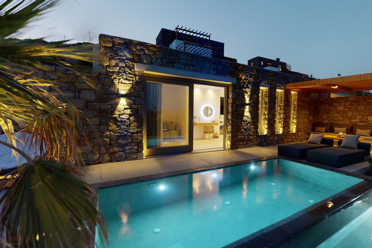 A modern house with a swimming pool, stone walls, and a well-lit interior.