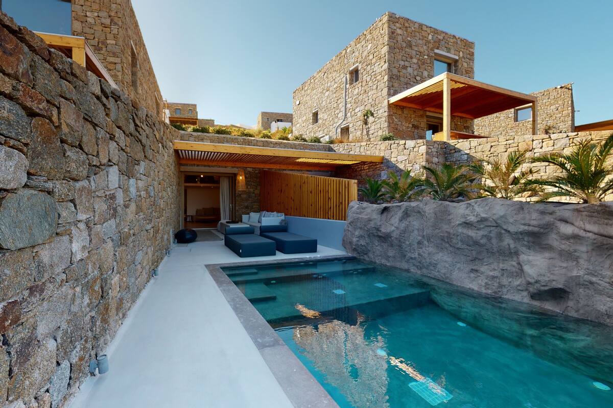 A stone-walled outdoor area with a pool, seating, and a view of a stone building.