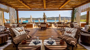 An outdoor seating area with tables and chairs, overlooking a coastal view. - Panormos Bay Suites (Mykonos)