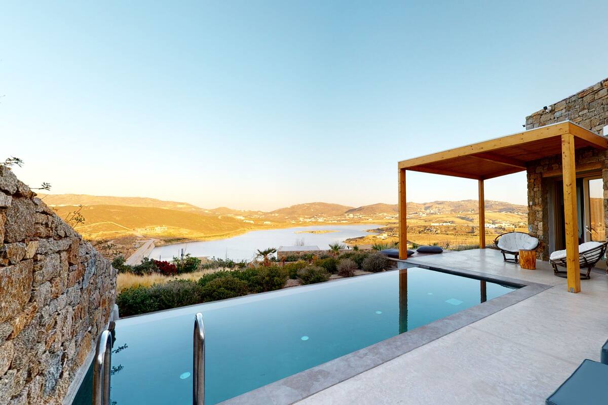 A modern outdoor pool area with a stone wall, wooden pergola, and lounge chairs.