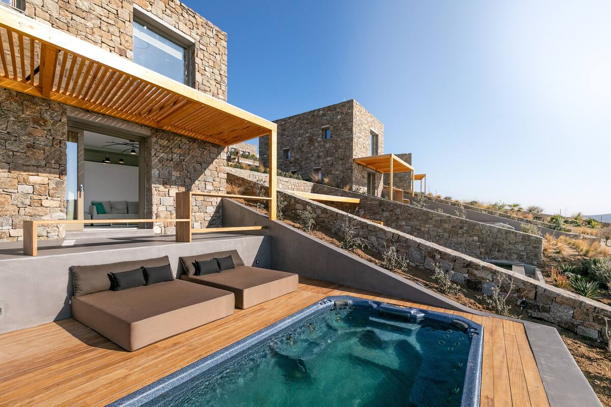 A modern outdoor pool area with a wooden deck, a built-in seating area, and a stone wall.