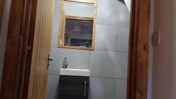 A bathroom with a wooden door, a mirror, a sink, and a window.