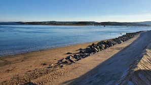 Une plage côtière avec un rivage rocheux, une eau calme et des collines qui se dessinent à l’horizon.
