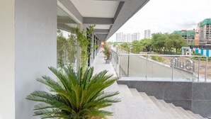 Um edifício moderno com área externa coberta, destacando uma escadaria, vasos de plantas e vista para a cidade.