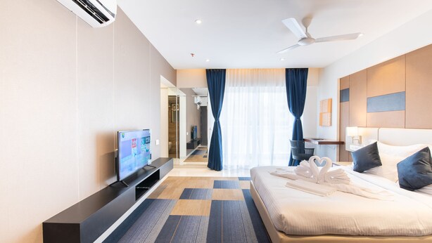 Quarto de hotel moderno com uma cama grande, uma TV de tela plana, um ventilador de teto e vista da cidade pela janela.