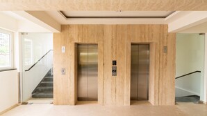 Área de elevadores com dois elevadores, escada e piso em tom claro.