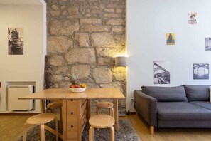 A room with a stone wall, a wooden table with a fruit bowl, a grey sofa, and a lamp.