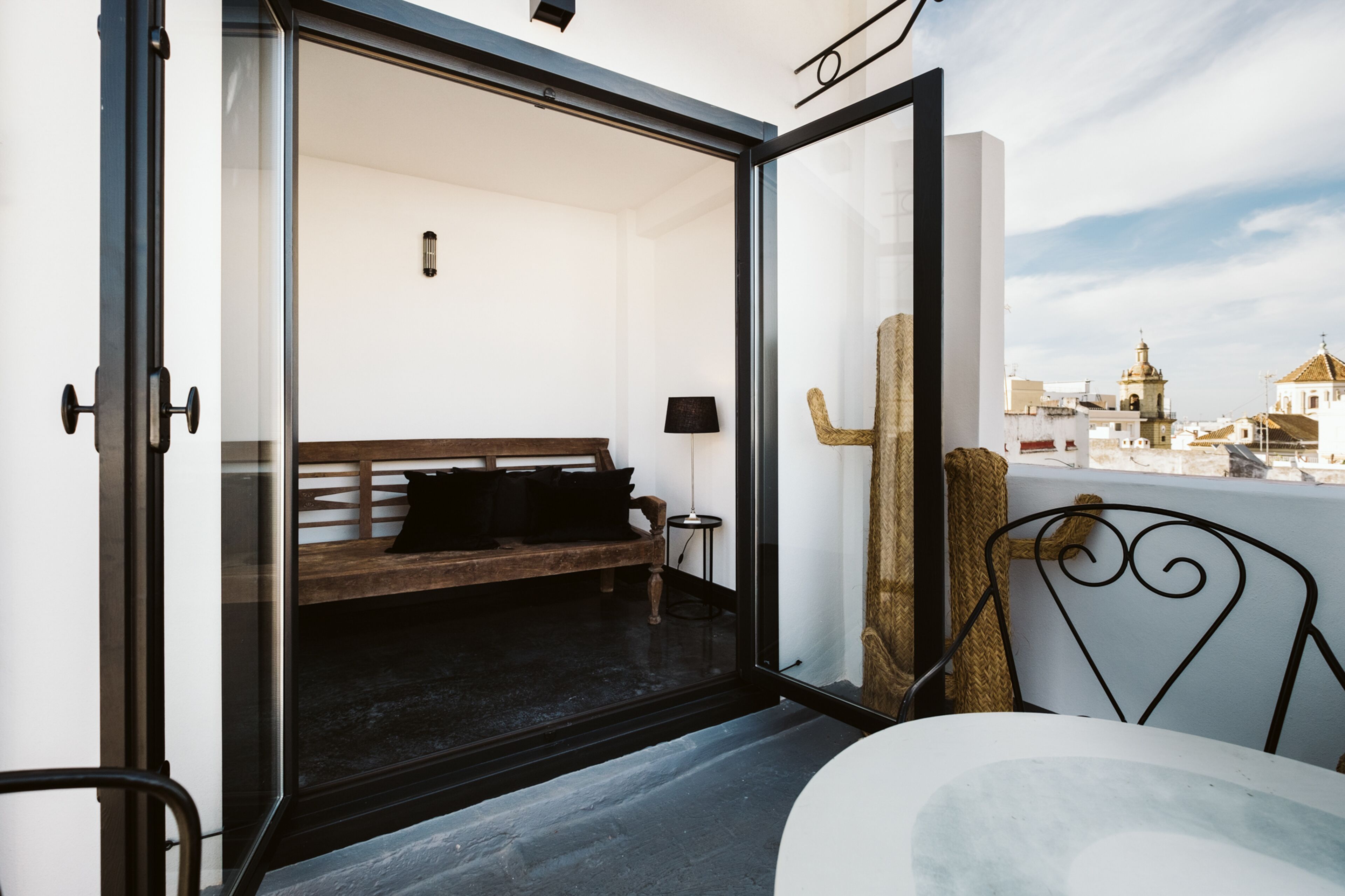 Un balcón con un banco de madera, una mesita y una silla de metal.