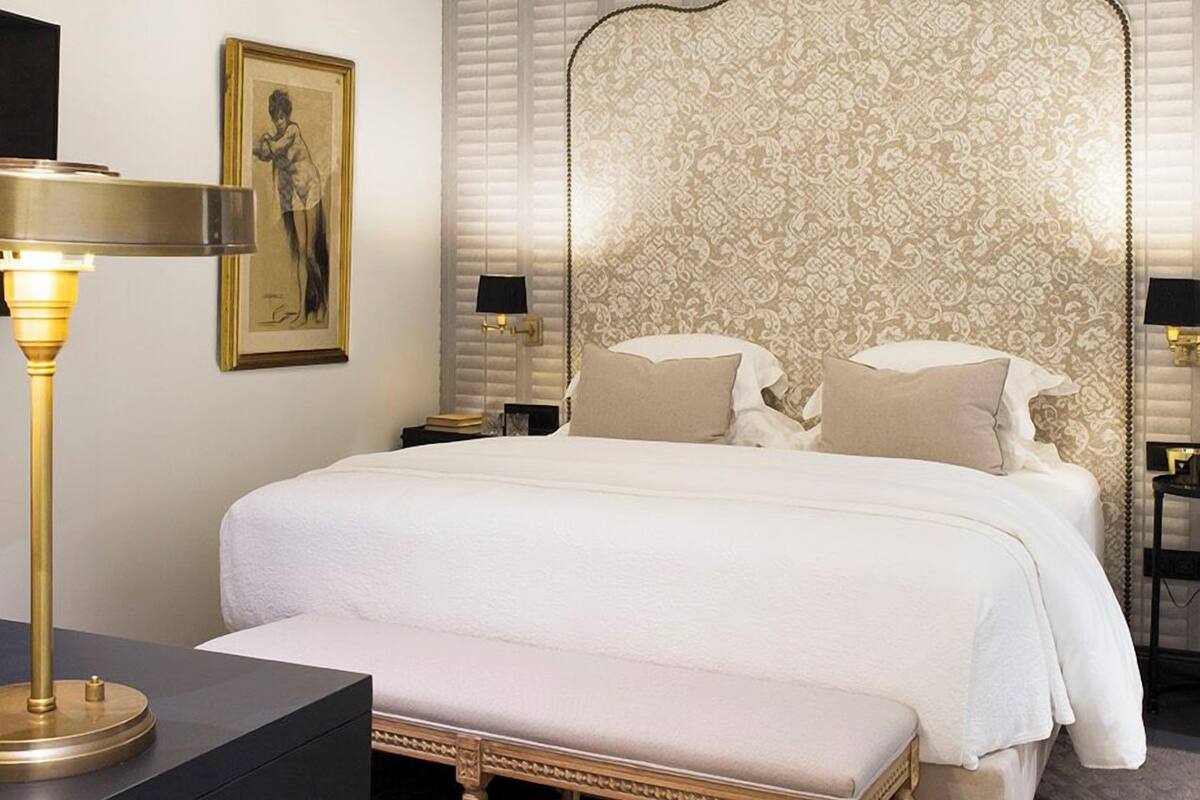 Una habitación de hotel con una cama grande, un candelabro, una mesita de noche, una lámpara y un cuadro en la pared.