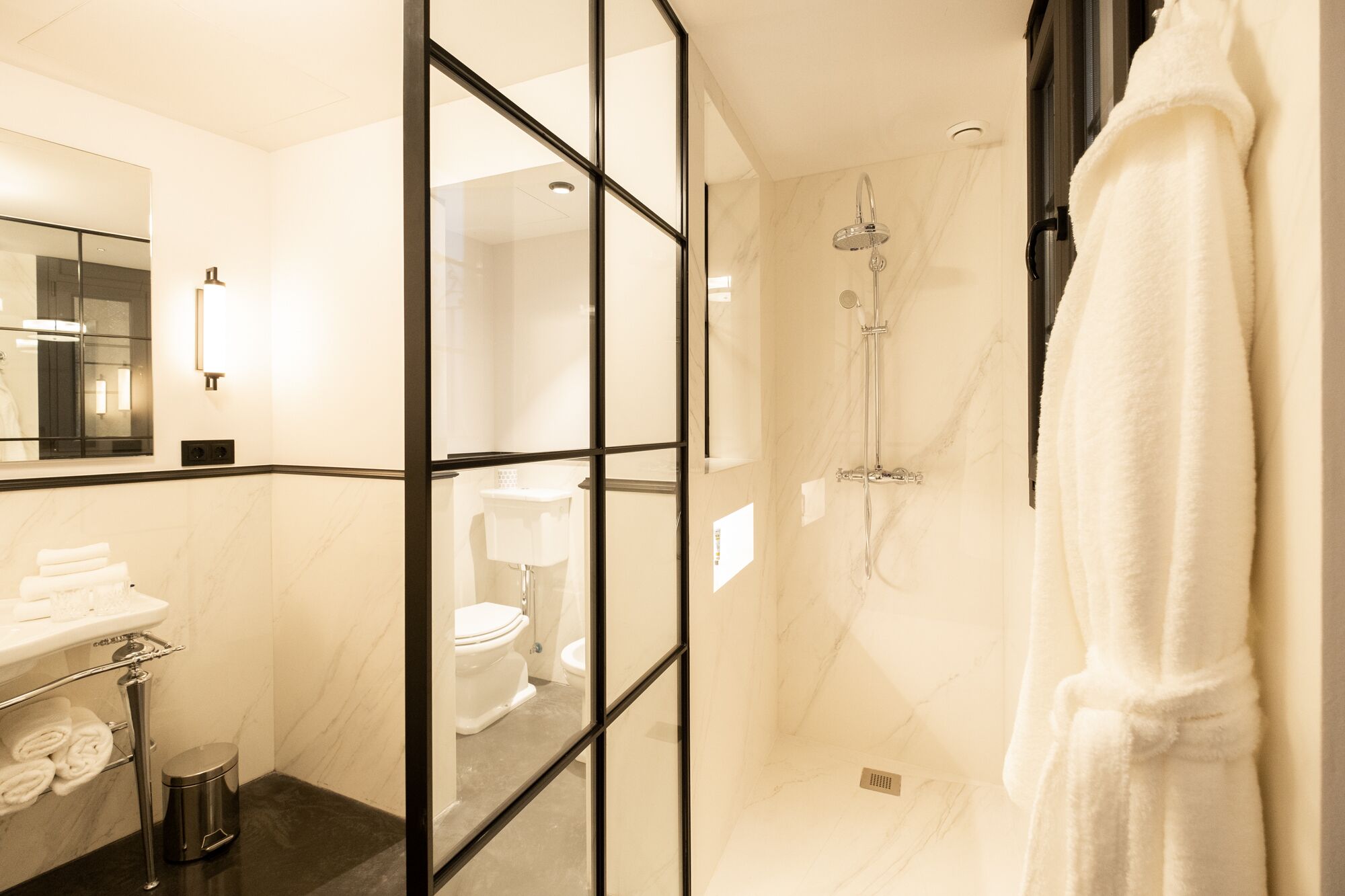 Un bany modern amb una cabina de dutxa de vidre, un vàter, un lavabo amb una barra per a tovalloles i un mirall gran.