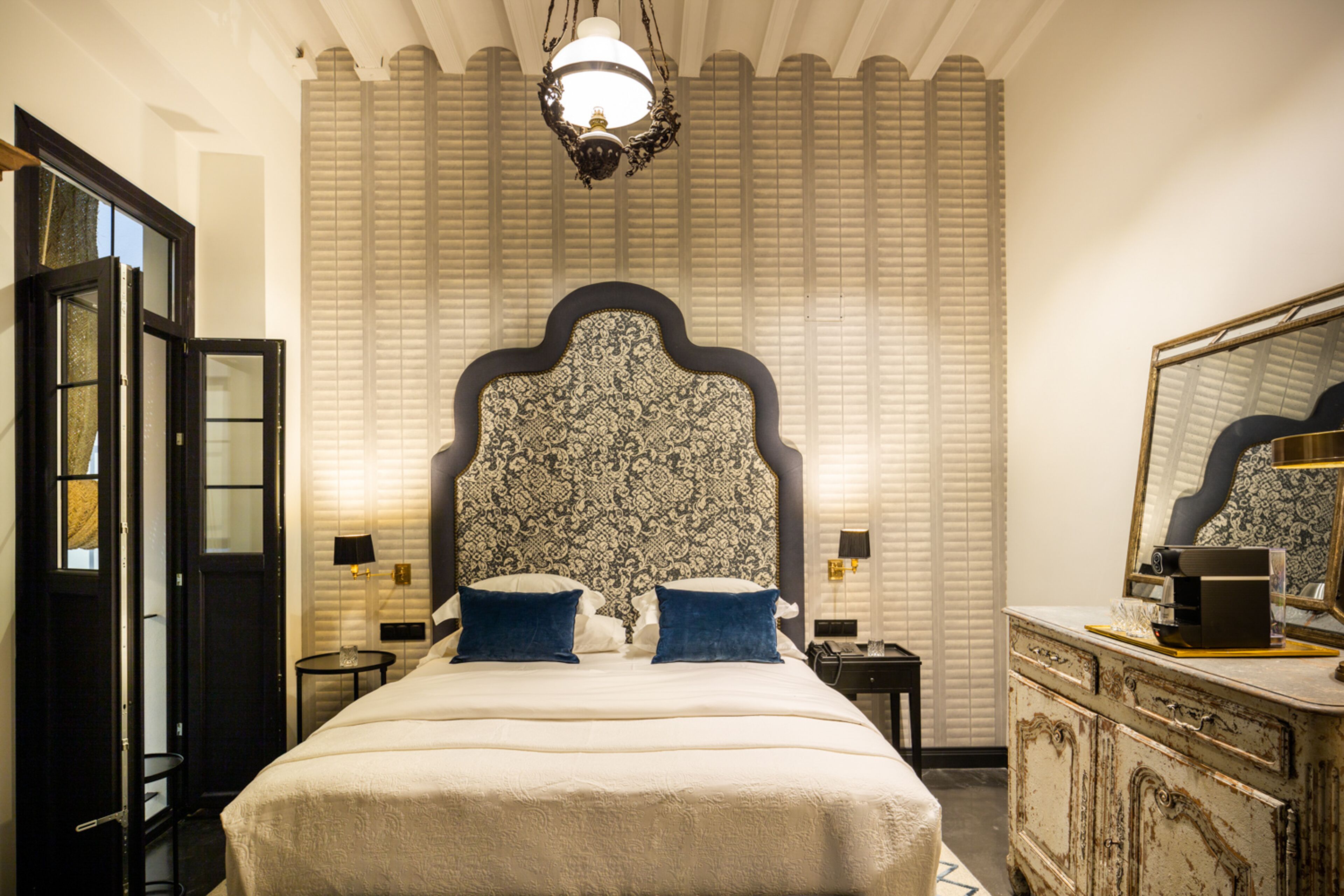 A bedroom with a large bed, a dresser, a mirror, and a chandelier.